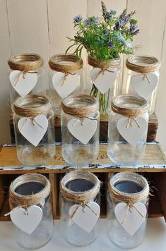 mason jars with heart tags and twine tied to them on a wooden shelf next to a potted plant