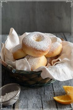 a basket filled with donuts covered in powdered sugar next to an orange slice