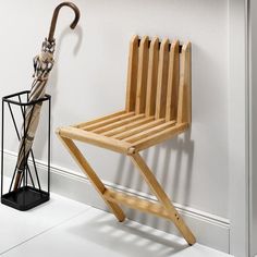 a wooden chair sitting next to an umbrella on top of a stand in front of a white wall