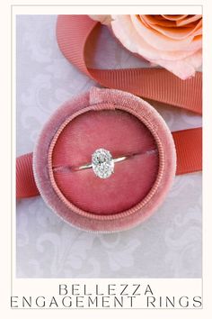 an engagement ring sits in a pink velvet box next to a rose and ribbon on a table