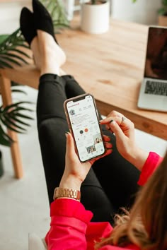 a woman is sitting on the couch and looking at her cell phone while she sits in front of a laptop