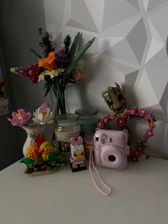 a white table topped with flowers and a pink camera next to a vase filled with flowers