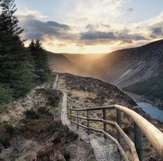 a wooden walkway leading to the top of a mountain with trees on both sides and a lake in the distance