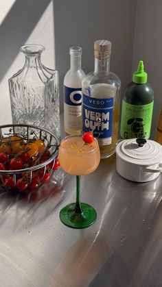 a metal counter topped with bottles and glasses next to a bowl filled with cherries