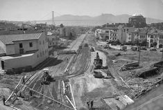 an old black and white photo of construction on the side of a road with buildings in the background