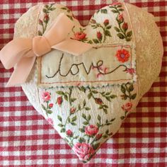 a heart shaped pillow with the word love written on it and a bow at the top