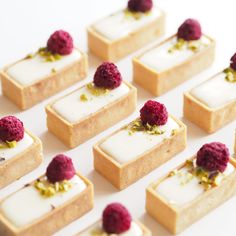 small desserts with raspberries are arranged in rows on a white tablecloth