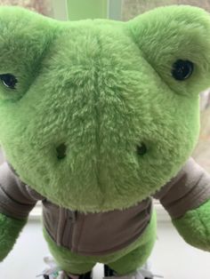 a green stuffed animal with black shoes on it's feet and one eye open