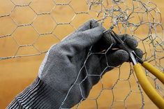 a gloved hand holding scissors near a chicken wire fence that has been placed on top of it