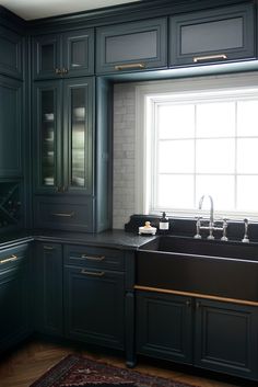 a kitchen with dark green cabinets and black counter tops, along with a rug on the floor