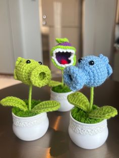 three crocheted flowers in white vases with green leaves and one blue flower