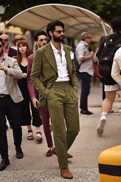 a man in a green suit and white shirt is walking down the street with other people