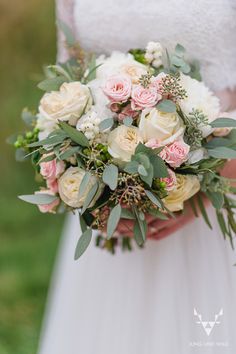 a bridal holding a bouquet of white and pink flowers with greenery on it