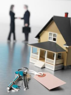 two people shaking hands in front of a house with keys on the table next to it