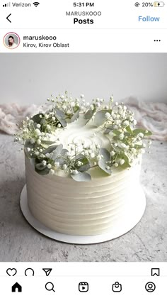 a white cake with flowers and greenery sitting on top of a table next to an instagram page