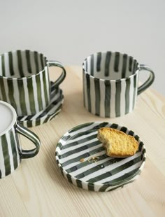 three cups and two plates with food in them on a wooden table next to each other