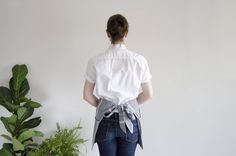 a woman standing in front of a potted plant wearing a white shirt and blue jeans