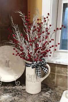 a white pitcher filled with red berries sitting on top of a counter next to a plate