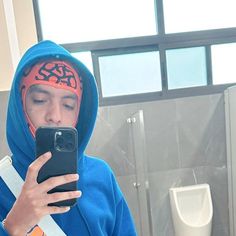 a man in a blue hoodie looking at his cell phone while standing in a bathroom