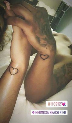 a woman laying on top of a bed with two hearts tattooed on her arm and leg