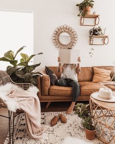 a woman sitting on a couch reading a book in her living room with potted plants