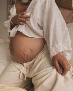 a pregnant woman sitting on top of a bed with her belly covered in sweats