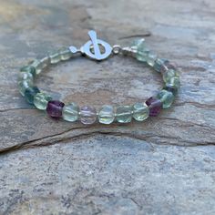 This fluorite bracelet features natural green and purple fluorite faceted in cube shape. Each cube is separated with a tiny silver bead. Strung on high quality beading wire and finished with a sterling silver Hill Tribe toggle clasp. A faceted green fluorite rondelle dangle sits near the clasp. 7.5 inch bracelet Please message me if you need a different size or clasp.  Cube size alone: 6mm To see more from East Village Jewelry~ http://eastvillagejewelry.etsy.com All orders ship out within 24 hours, excluding holidays and Sundays Feel free to contact me with any questions. Use coupon code VILLAGE14 for 10% off all orders over $200.00 THIS ITEM WILL SHIP OUT WITHIN 24 HOURS OF ORDERING FREE SHIPPING WITHIN THE UNITED STATES! Fluorite Gemstone Bracelets With Round Beads, Fluorite Bracelets, Silver Fluorite Jewelry With Natural Stones, Handmade Adjustable Fluorite Bracelets, Sunday Feels, Purple Fluorite Gemstone Necklace, Fluorite Bracelet, Cube Shape, Purple Fluorite