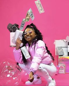 a woman kneeling on the ground in front of a pink background with money flying out of her mouth