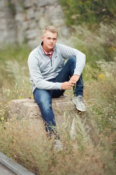 a young man sitting on top of a rock in the middle of some tall grass