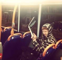 a young man sitting on a bus holding a laptop