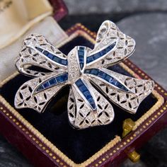 This stunning bow brooch pin features a pierced bow with milgrain details.  The brooch is bead set with forty-five (45) round brilliant cut diamonds, and channel set with thirty-one square and triangle step cut sapphires.  The brooch measures 31.4mm tall by 36.5mm wide by 4.7mm deep.  It is finished with a hinged locking pin back. Elegant Brilliant Cut Brooches As Gifts, Diamond Brooches With Brilliant Cut For Gift, Brilliant Cut Diamond Brooches For Gift, Luxury Platinum Brooches As Gift, Elegant Platinum Brooches For Gift, Elegant Brilliant Cut Brooches For Anniversary, Elegant Diamond White Brooches As Gifts, Elegant Diamond White Brooches For Gift, Fine Jewelry Brooches With Diamond Accents For Gifts