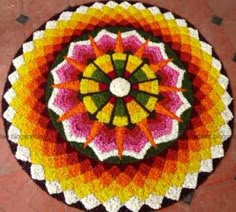 a circular crocheted rug with an orange, yellow and pink flower on it