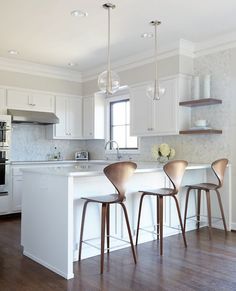 three bar stools sit at the center of a kitchen island in front of an oven