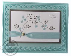 a card with a blue ribbon and some flowers on the front, and an embellishment that says thinking of you