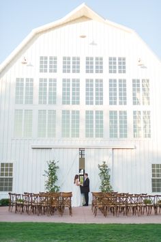 a bride and groom standing in front of a large white barn with tables set up for their wedding ceremony