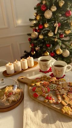 a christmas tree is in the background with cookies and coffee cups on a table next to it