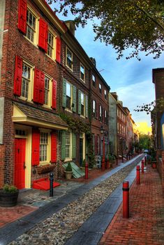 a row of brick buildings with red shutters on the doors and windows, along a cobblestone street