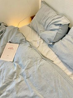 an unmade bed with blue and white sheets, pillows and a book on it