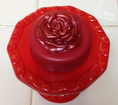 a red candle holder with a rose on it's lid sitting on a white tile floor