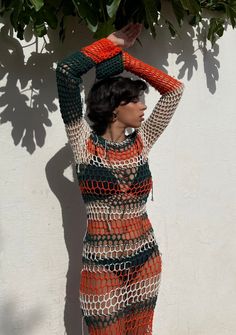 a woman in an orange and black crochet dress is leaning against a white wall