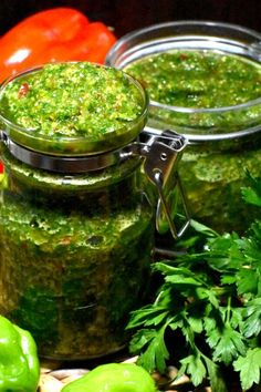 two jars filled with pesto next to green peppers