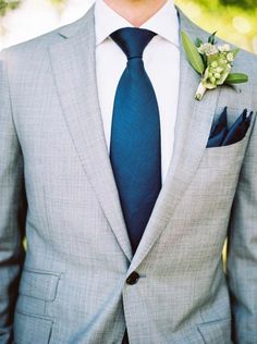 a man in a gray suit with a blue tie and flower boutonniere