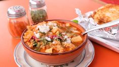 a bowl of soup sits on a plate next to some bread and seasoning shakers