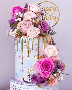 a blue and pink cake with gold icing and flowers on the top is sitting on a table