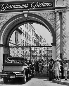 an old black and white photo of people standing in front of a gated entrance