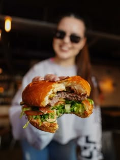 a woman holding up a large sandwich with meat and lettuce in it's hand