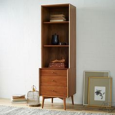 a wooden bookcase sitting next to a white wall and a bird cage on the floor