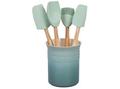 the toothbrush holder has five mint green plastic brushes in it and is holding four wooden spoons