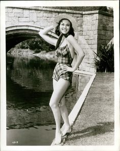 an old photo of a woman posing in front of a bridge wearing a bathing suit