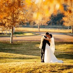 a bride and groom standing in the grass at their fall wedding ceremony, hugging each other